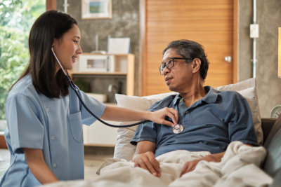Female doctor checking the health of Asian elderly male patient at home