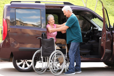 Mature man helping senior women to get out from van into wheelchair outdoors