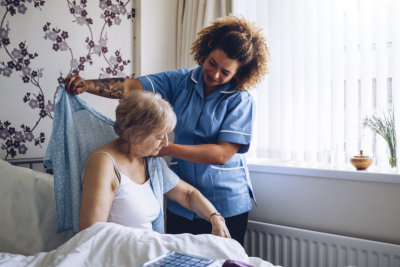 Home Caregiver helping a senior women get dressed in her bedroom